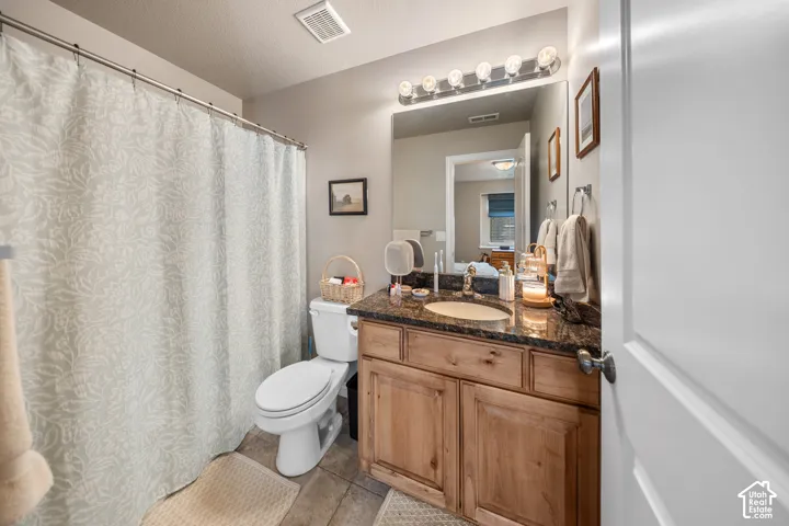 Bathroom featuring a wood vanity with a dark-toned stone countertop, integrated oval sink, full-width wall mirror, and multi-bulb vanity lighting