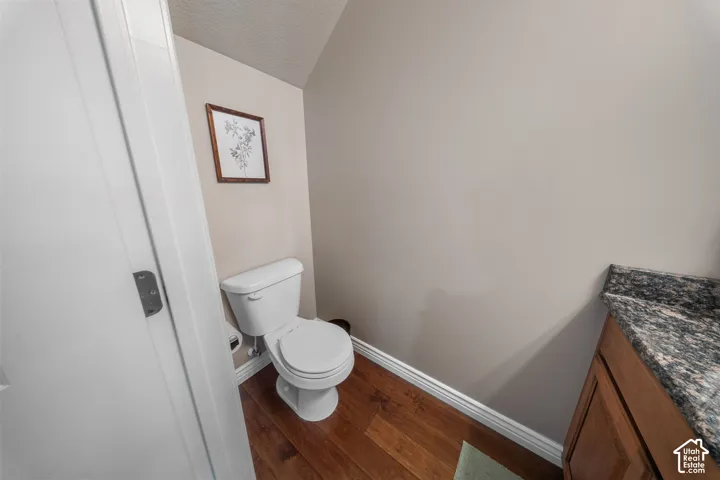 Bathroom featuring a wood-finish vanity with a stone-composite countertop, white porcelain toilet, and wood-finish flooring
