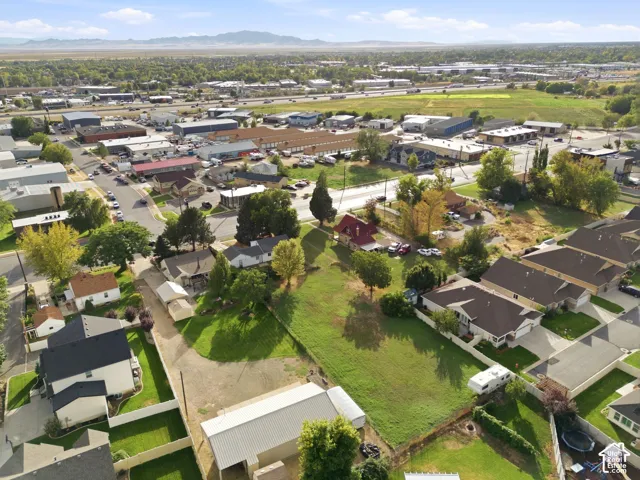 Aerial perspective of a sprawling lot featuring expansive grass grounds, mature trees, a detached metal-roofed structure, and a mountainous horizon