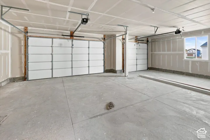 Three-car garage featuring finished drywall, two overhead garage door openers, and a concrete floor