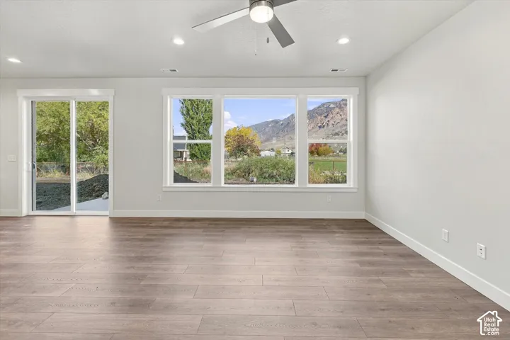 Open-concept interior featuring wood-finish flooring, a ceiling fan, recessed lighting, expansive triple-pane windows, and a sliding glass door providing exterior access