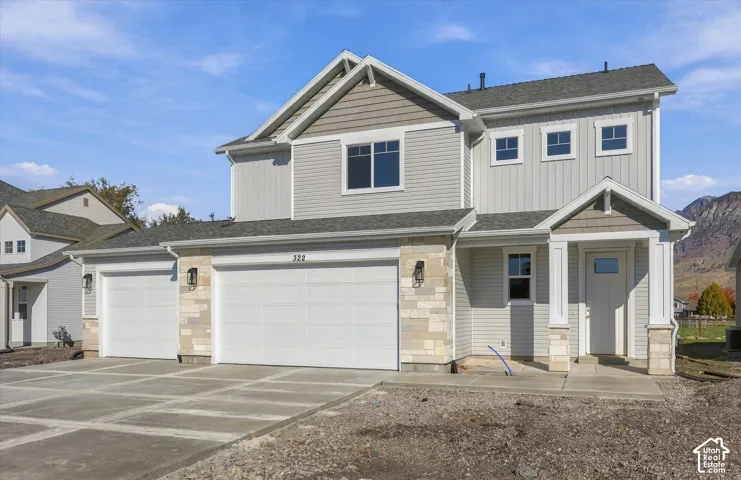 Two-story exterior featuring horizontal and vertical siding, stone veneer accents, a multi-car garage, and a covered front porch with square columns