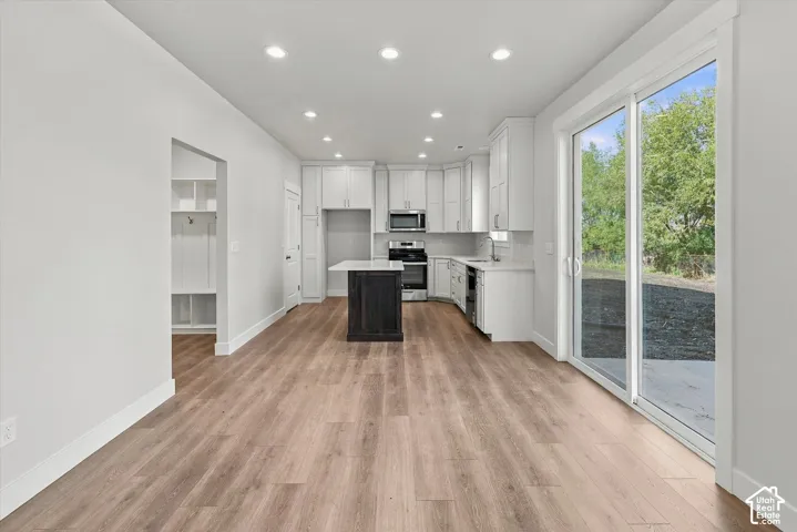 Kitchen featuring white shaker cabinetry, a contrasting dark-finish center island, recessed ceiling lighting, wood-finish flooring, and a large sliding glass door