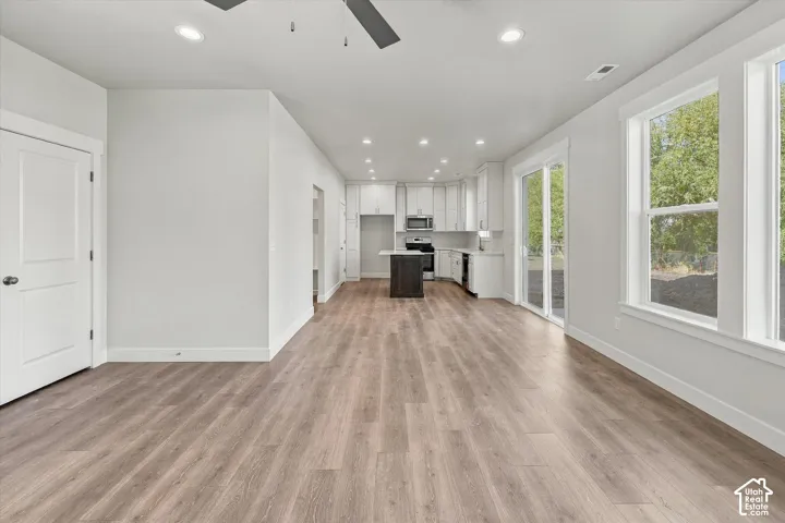 Open-concept kitchen featuring white shaker-style cabinetry, an island with a contrasting dark finish, wood-finish flooring, and sliding glass doors