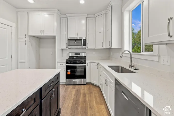 Kitchen featuring white shaker-style cabinetry, a contrasting dark-finish kitchen island, solid-surface countertops, stainless steel appliances, and wood-finish flooring