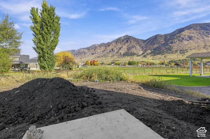 Expansive lot featuring a concrete patio pad, metal perimeter fencing, manicured lawn areas, and a prominent mountain backdrop