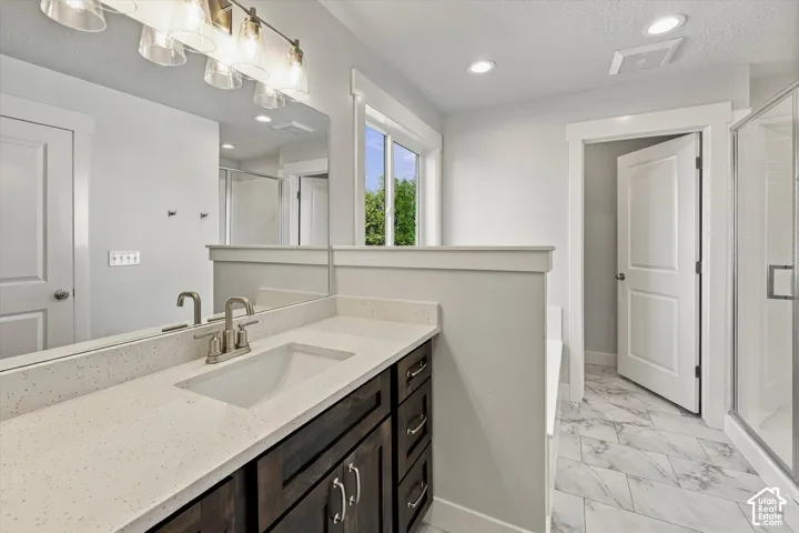 Dark wood-finish cabinetry, light-toned stone-finish countertop with an integrated basin, multi-light vanity fixture, and large-format tile flooring