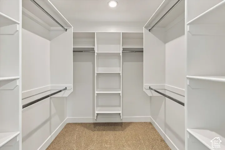 Walk-in closet featuring white built-in shelving, multiple hanging rods, and neutral carpeting