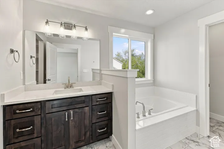 Bathroom featuring dark wood cabinetry, a light-toned solid surface countertop, a tiled soaking tub, and stone-finish flooring