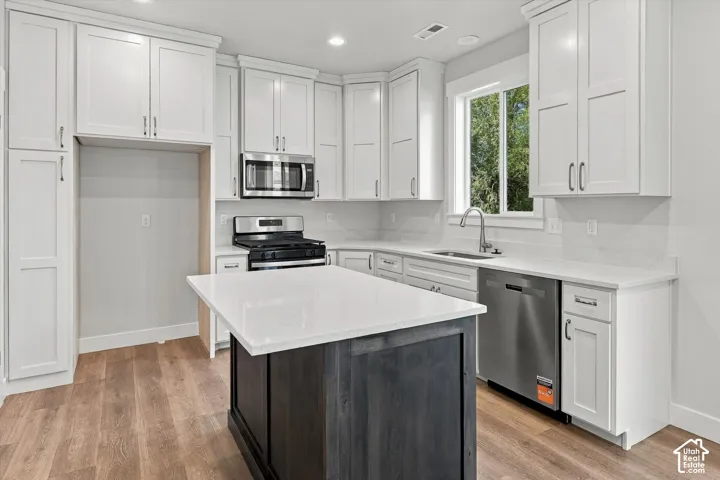 Kitchen featuring white shaker-style cabinetry, quartz countertops, a contrasting dark-finish center island, stainless steel appliances, and wood-finish flooring