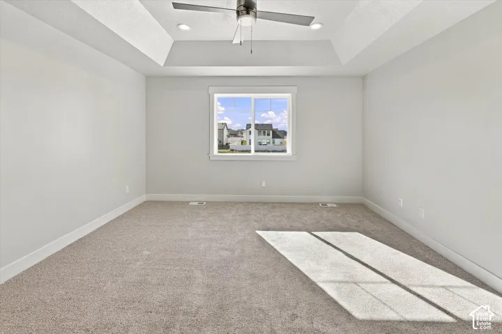 Tray ceiling with recessed lighting, central ceiling fan, carpeted flooring, and neutral wall tones