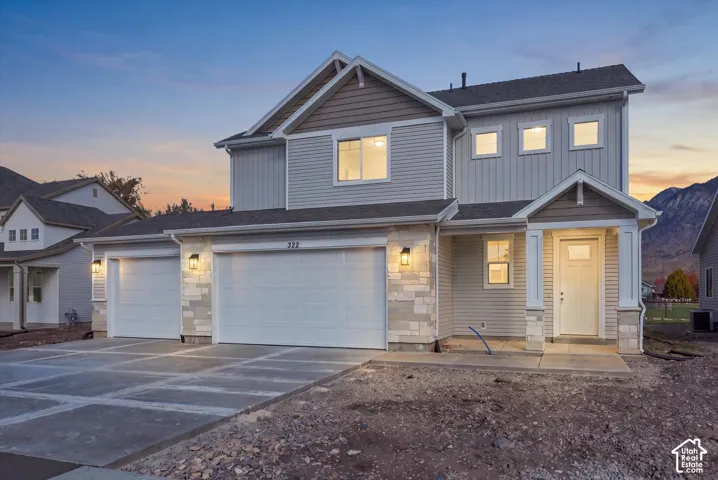 Two-story exterior featuring stone veneer accents, horizontal and vertical siding, a three-car garage, and a covered front porch entry