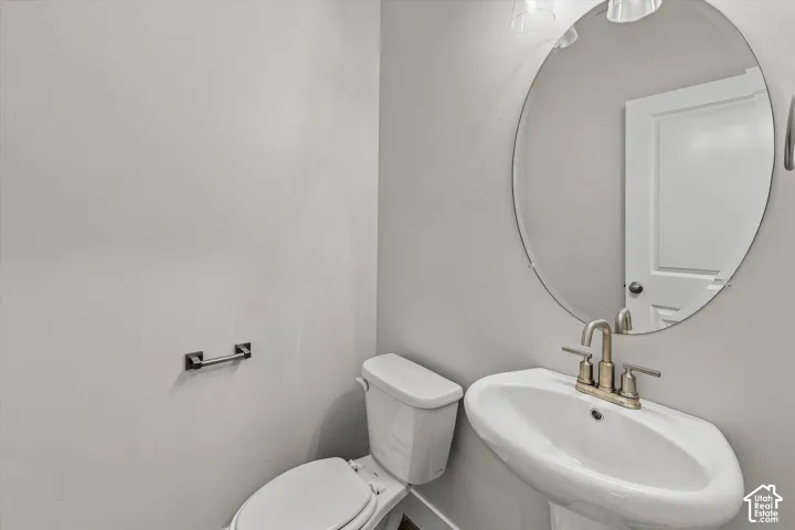 Pedestal sink with metallic widespread faucet, oval wall-mounted mirror, two-piece toilet, and three-light fixture