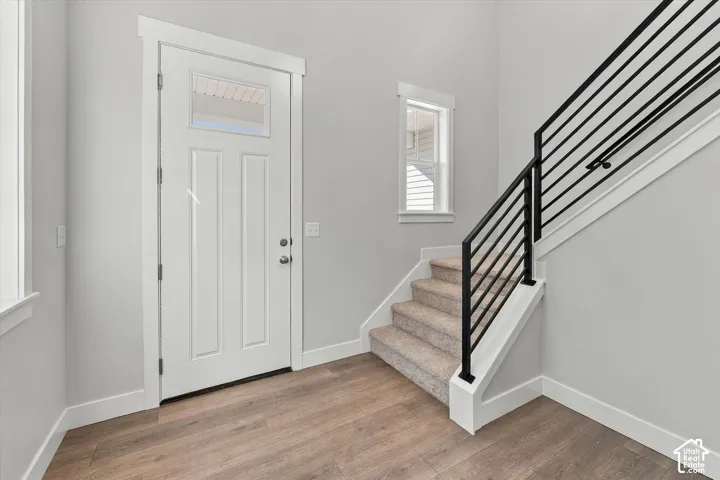 Entryway featuring wood-finish flooring, a white paneled door with glass transom, carpeted staircase, and matte black horizontal metal railing