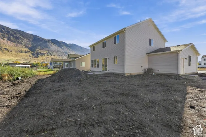 Two-story residential structure featuring light-colored horizontal siding, a concrete rear patio, and a mountain backdrop
