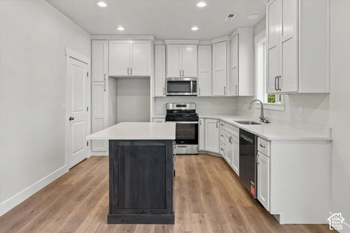 Kitchen featuring white shaker-style cabinetry, quartz countertops, a dark-toned center island, recessed lighting, and wood-finish flooring