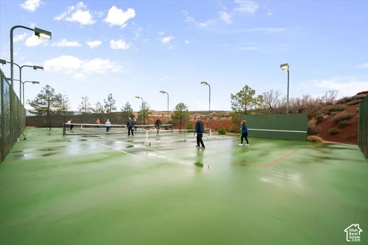 Outdoor tennis court featuring a hard surface, perimeter chain-link fencing, and installed overhead lighting