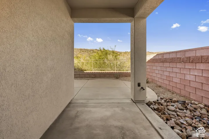 Covered concrete patio featuring a textured stucco finish, decorative stone landscaping, and a masonry perimeter wall