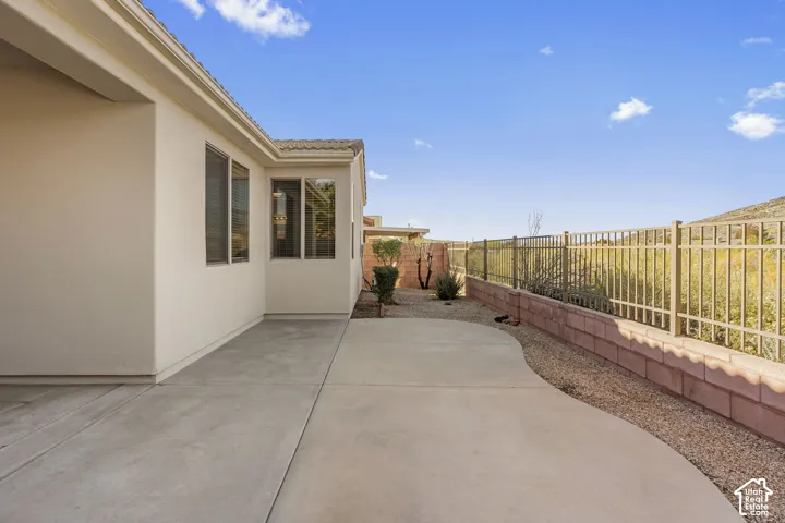 Rear patio featuring concrete surfacing, stucco exterior, metal fencing, and decorative stone walling