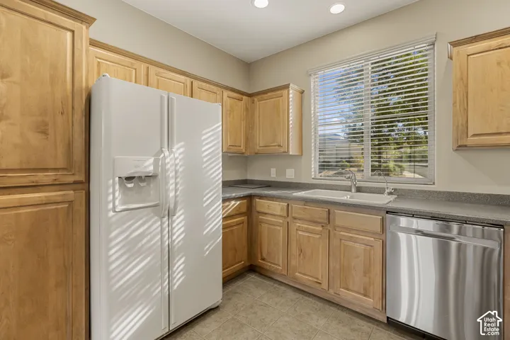 Kitchen featuring natural-finish wood cabinetry, solid-surface countertops, integrated double-basin sink, stainless steel dishwasher, and matching white full-size refrigerator