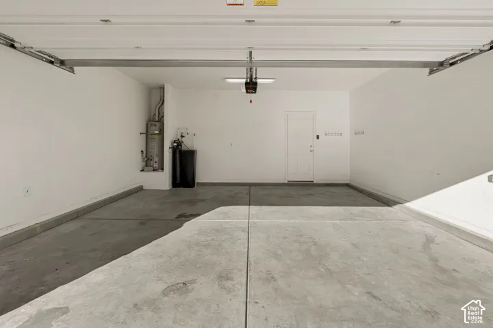 Finished garage space featuring smooth concrete flooring, white walls, an integrated water heating system, water softener, and a dedicated service door