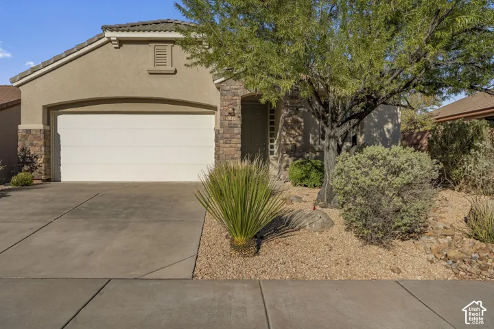 Stucco exterior featuring stone veneer accents, concrete driveway, tiled roof, and desert-inspired landscaping