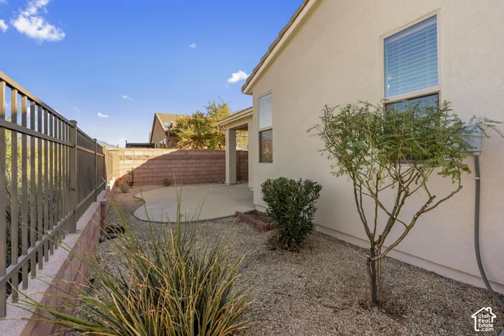 Stucco exterior featuring a concrete patio, decorative metal fencing, stone-composite perimeter wall, and gravel ground cover