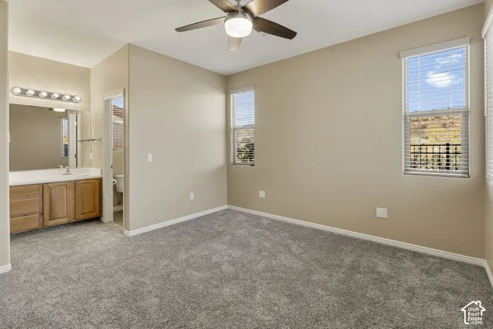 Neutral-toned interior featuring wall-to-wall carpeting, wood-finish cabinetry, a lighted ceiling fan, and windows with horizontal blinds