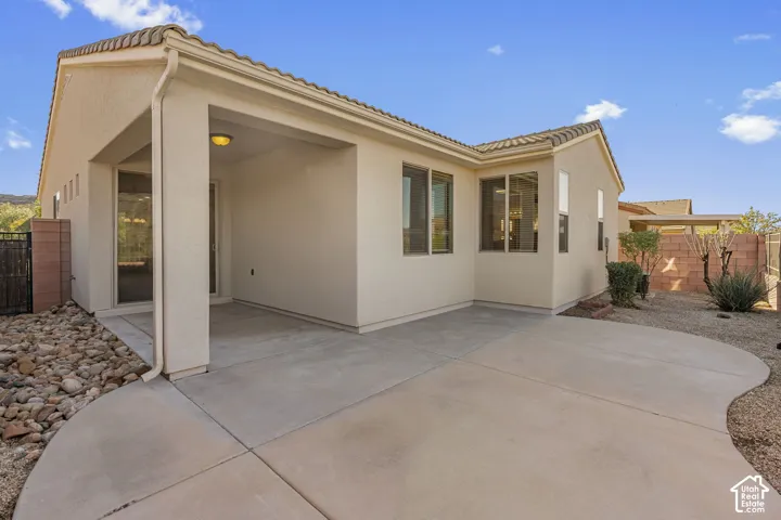 Stucco exterior featuring a covered patio, concrete hardscaping, tile roof, and desert-inspired landscape rock
