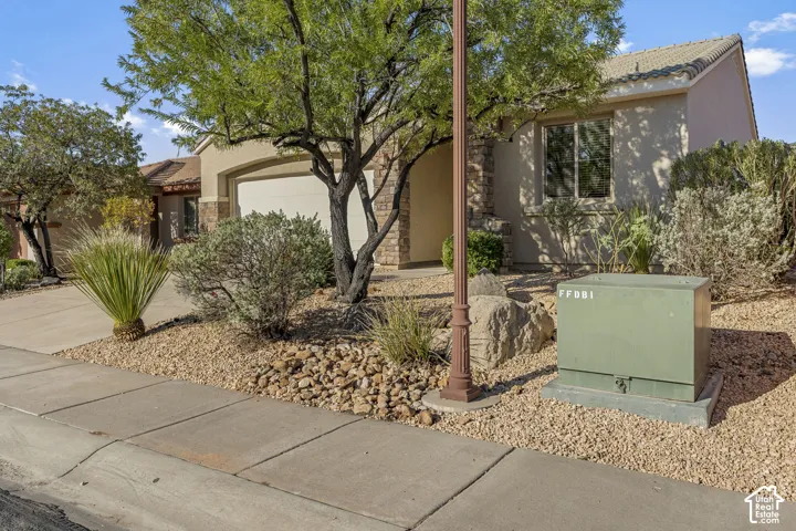 Stucco exterior featuring stone masonry accents, tile roofing, a concrete driveway, and xeriscaped front grounds