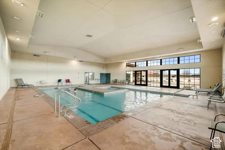 Indoor swimming pool area featuring a built-in spa, concrete tile flooring, high vaulted ceilings, and expansive glass-paneled walls