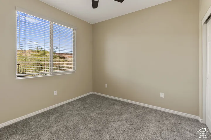 Carpeted room featuring a large window, neutral wall paint, a ceiling fan, and a built-in closet with sliding doors