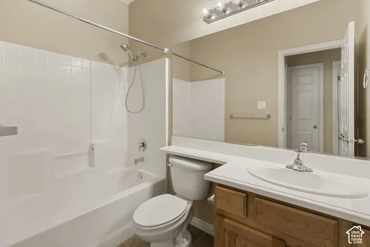 Bathroom featuring a wood-finish vanity with a white countertop, oval drop-in sink, shower-tub combination with white surround, and a full-width vanity mirror