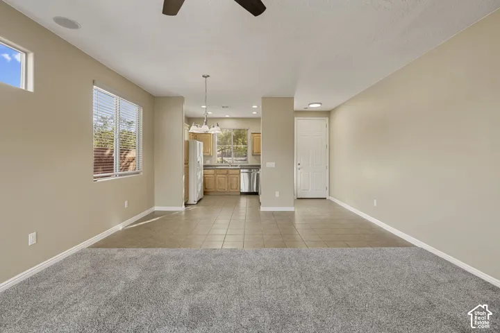 Interior space featuring wall-to-wall carpeting, neutral-toned paint, tile flooring in the kitchen area, wood cabinetry, and a ceiling fan
