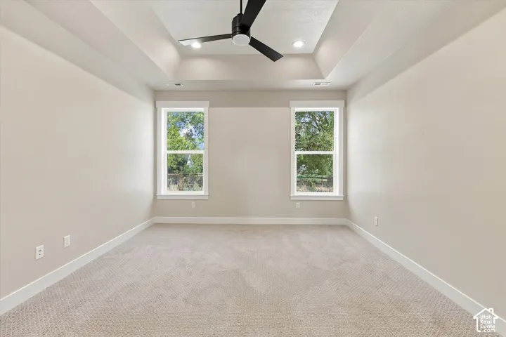 Tray ceiling with a central matte black ceiling fan, recessed lighting, neutral carpeting, and dual windows
