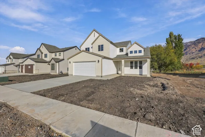 Two-story residence featuring a stucco and siding exterior, multi-gabled roofline, attached two-car garage, concrete driveway, and mountain backdrop