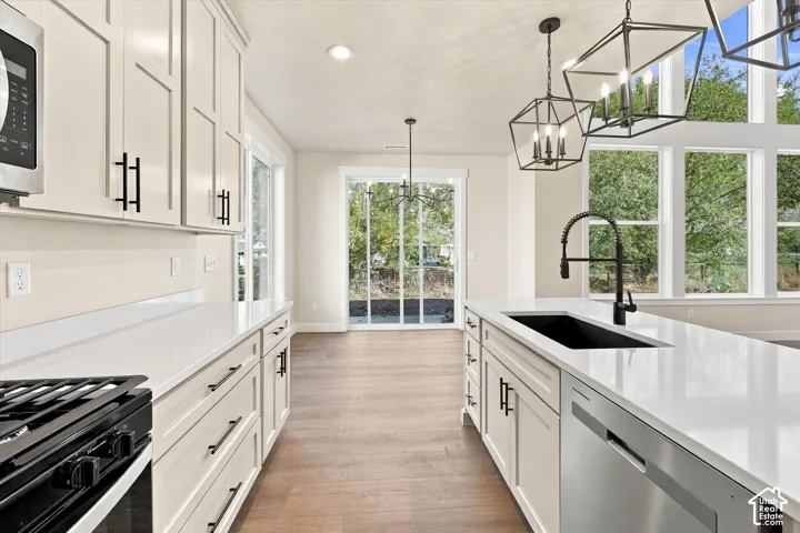 Kitchen featuring shaker-style cabinetry, quartz countertops, a matte black faucet with an integrated undermount sink, multi-tier geometric pendant lighting, and wood-finish flooring
