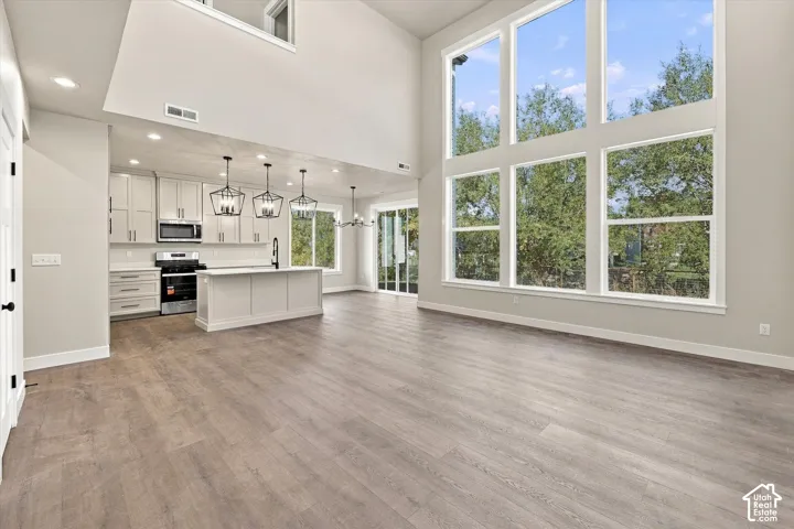 Expansive floor-to-ceiling windows, soaring vaulted ceilings, wood-finish flooring, kitchen island with built-in cabinetry, and pendant light fixtures
