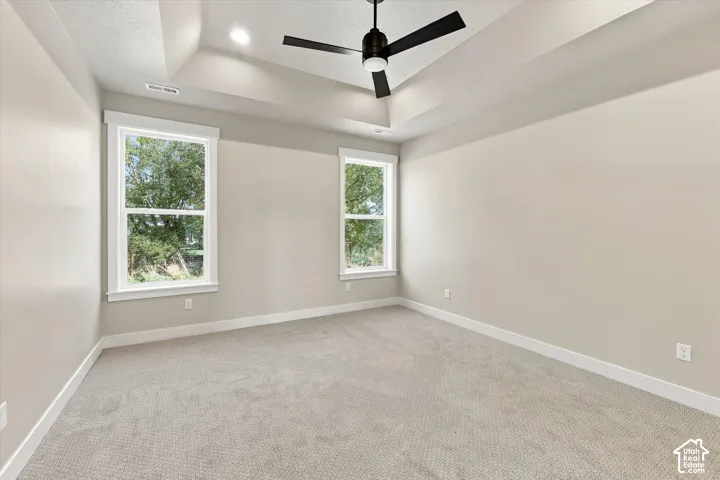 Tray ceiling featuring a matte black finish ceiling fan, neutral wall-to-wall carpeting, and double-pane windows with white casing