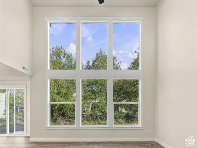 High-ceiling interior featuring expansive multi-pane windows, wood-finish flooring, recessed lighting, and a modern ceiling fan
