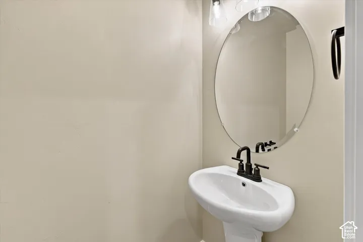 Wall-mounted oval frameless mirror, white pedestal sink, oil-rubbed bronze centerset faucet, and coordinating oil-rubbed bronze towel ring
