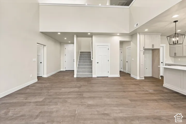 Open-concept interior featuring wood-finish flooring, high ceilings, recessed lighting, shaker-style cabinetry, and a geometric pendant light fixture