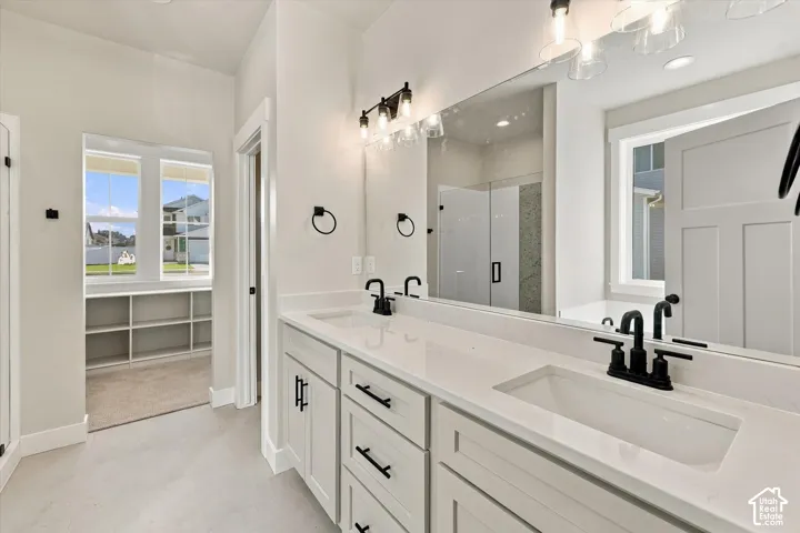 Dual-sink vanity with white stone-composite countertop, matte black fixtures, full-width vanity mirror, custom shaker-style cabinetry, and recessed lighting