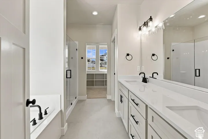 Dual-sink vanity with quartz countertops, matte black fixtures, glass-enclosed shower, soaking tub, and custom built-in cabinetry