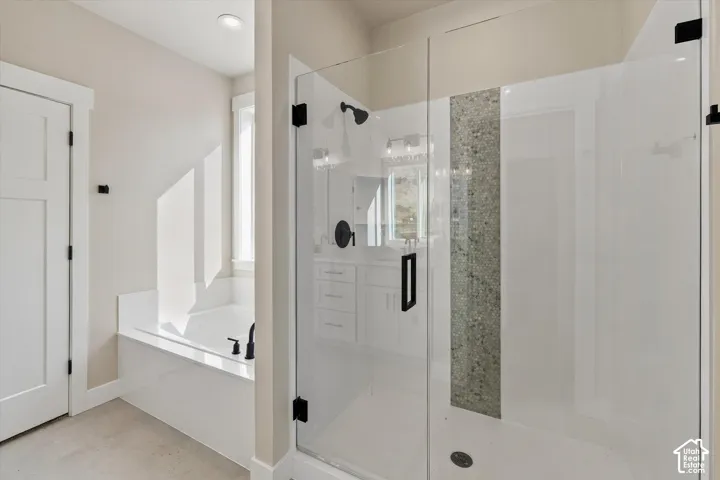 Walk-in shower with a glass enclosure, decorative stone-finish tile inlay, and matte black hardware, accompanied by a deep-basin soaking tub with a matching matte black deck-mounted faucet