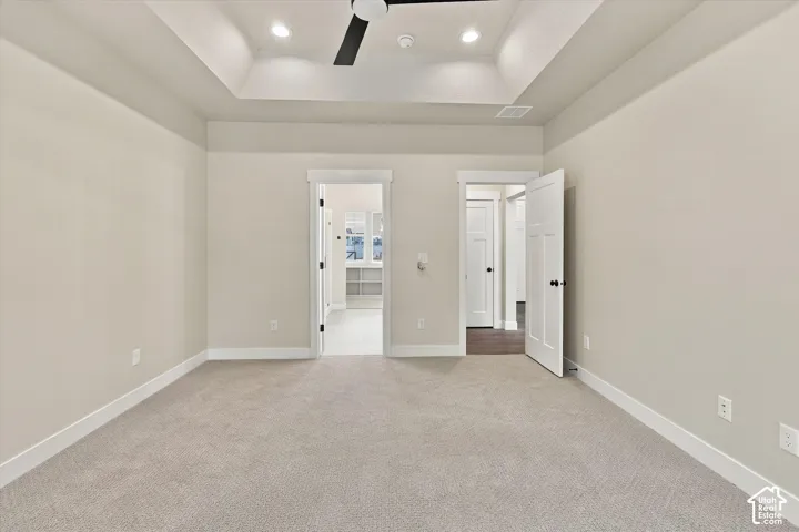 Tray ceiling featuring recessed lighting and a ceiling fan, neutral wall-to-wall carpeting, and solid-core paneled interior doors