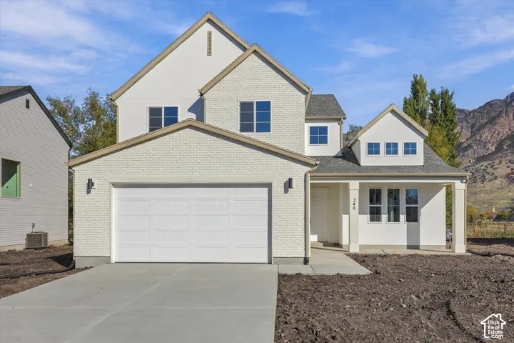 Multi-level residence featuring painted brick and stucco exterior, gable rooflines, two-car garage, covered entryway, and mountain backdrop