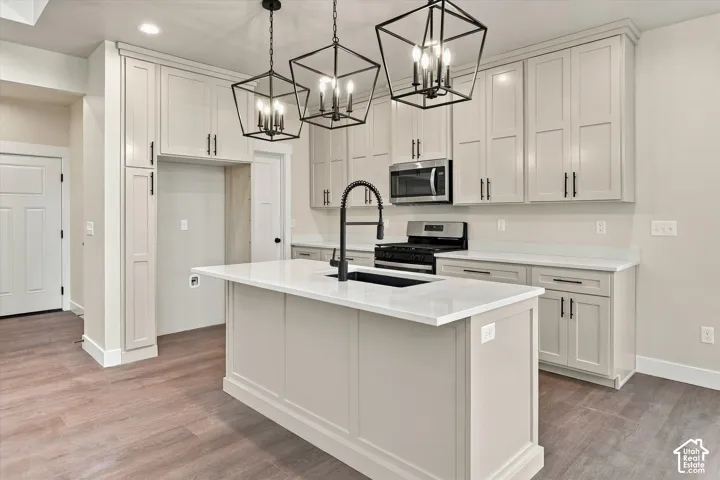 Kitchen featuring Shaker-style cabinetry, a central island with a quartz countertop, matte black hardware, geometric pendant lighting, and wood-finish flooring
