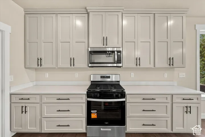 Shaker-style cabinetry featuring a light neutral finish and matte black hardware, paired with light-toned solid surface countertops and a stainless steel built-in microwave and gas range