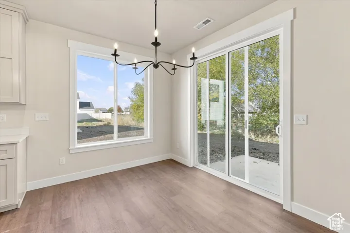 Dining space featuring wood-finish flooring, a five-arm metal chandelier, large windows, and glass sliding doors providing exterior access